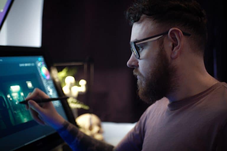 Mockup of a young man working on digital art on a tablet in a dark room, focusing on game development, digital illustration, concept art, creative process, using stylus and graphics tablet for design work, studio environment, professional 3D or 2D game art production.